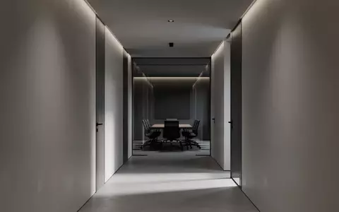 Ein minimalistischer, unbelebter Büroflur mit klaren Linien und geometrischen Schatten, der eine ruhige und professionelle Arbeitsumgebung darstellt. - Foto: über boerse-global.de