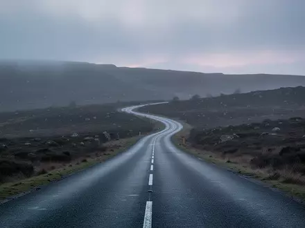 Eine einsame, sich durch eine neblige Hügellandschaft schlängelnde Asphaltstraße bei Dämmerung. - Foto: über boerse-global.de