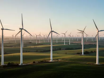 Moderne Windkraftanlagen in einer weitläufigen grünen Landschaft bei Sonnenaufgang. - Foto: über boerse-global.de