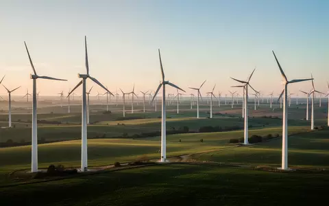 Moderne Windkraftanlagen in einer weitläufigen grünen Landschaft bei Sonnenaufgang. - Foto: über boerse-global.de