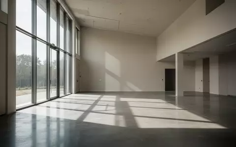 Ein minimalistischer, leerer Gebäuderaum mit natürlichem Lichteinfall und geometrischen Schatten auf einem Betonboden. - Foto: über boerse-global.de