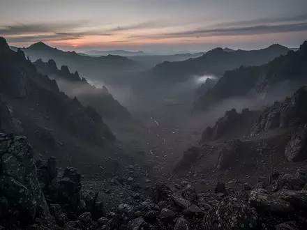 Eine weitläufige, einsame Berglandschaft in der Dämmerung, die von einem erhöhten Aussichtspunkt über ein leeres Tal blickt. - Foto: über boerse-global.de