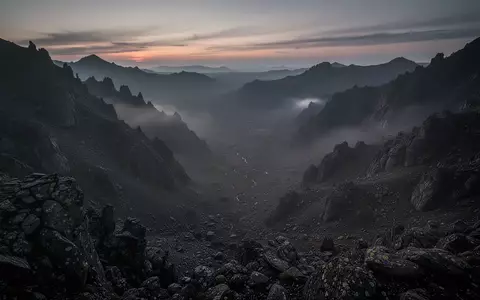 Eine weitläufige, einsame Berglandschaft in der Dämmerung, die von einem erhöhten Aussichtspunkt über ein leeres Tal blickt. - Foto: über boerse-global.de
