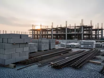 Baustelle mit ordentlich aufgeschichteten Baumaterialien und einem Rohbau im Hintergrund bei Tagesanbruch. - Foto: ĂŒber boerse-global.de