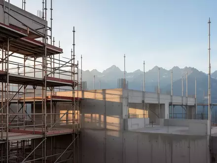 Rohbau einer Baustelle mit StahlgerĂĽst vor einer Bergkulisse bei Tageslicht. - Foto: ĂĽber boerse-global.de