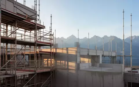 Rohbau einer Baustelle mit StahlgerĂĽst vor einer Bergkulisse bei Tageslicht. - Foto: ĂĽber boerse-global.de