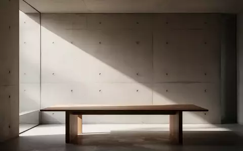 Ein minimalistischer, lichtdurchfluteter Raum mit einer schlichten Betonwand und einem leeren Holztisch in einer ruhigen Atmosphäre. - Foto: über boerse-global.de