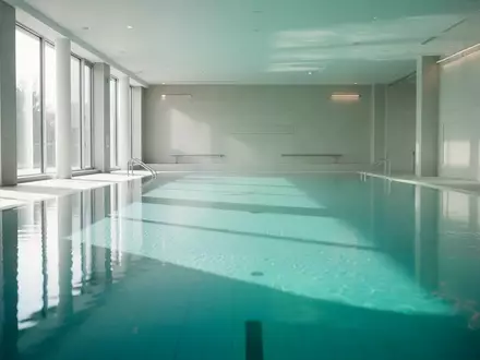 Ein helles, modernes Hallenbad mit ruhiger Wasseroberfläche und minimalistischer Architektur ohne Personen. - Foto: über boerse-global.de