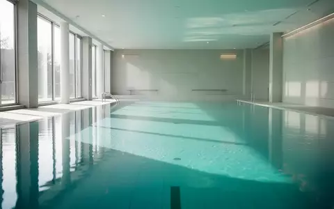 Ein helles, modernes Hallenbad mit ruhiger Wasseroberfläche und minimalistischer Architektur ohne Personen. - Foto: über boerse-global.de