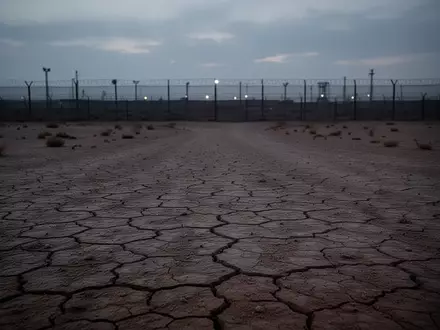 Eine weite, einsame Wüstenlandschaft mit einem fernen Grenzzaun in der Dämmerung. - Foto: über boerse-global.de