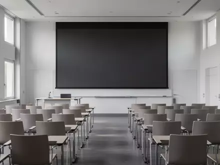 Ein leerer, modern gestalteter medizinischer Hörsaal in München mit Blick auf eine dunkle Projektionsfläche. - Foto: über boerse-global.de