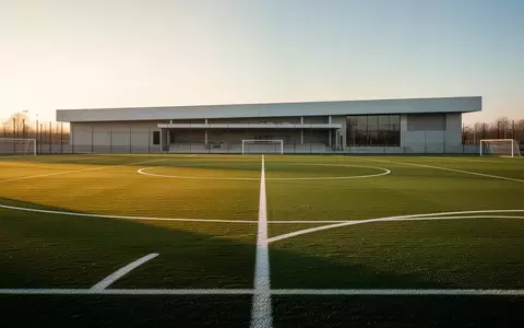 Ein leerer, professionell gepflegter Fußballplatz bei Sonnenuntergang mit einem modernen Sportgebäude im Hintergrund. - Foto: über boerse-global.de