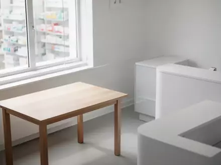 Ein heller, minimalistischer Beratungsbereich in einer Apotheke mit einem leeren Holztisch und neutralem Hintergrund. - Foto: über boerse-global.de