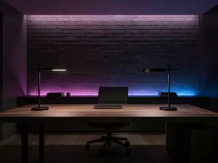 Ein modern gestalteter, minimalistischer Arbeitsplatz mit dunklem Holzschreibtisch und dezenter, stimmungsvoller Beleuchtung. - Foto: über boerse-global.de