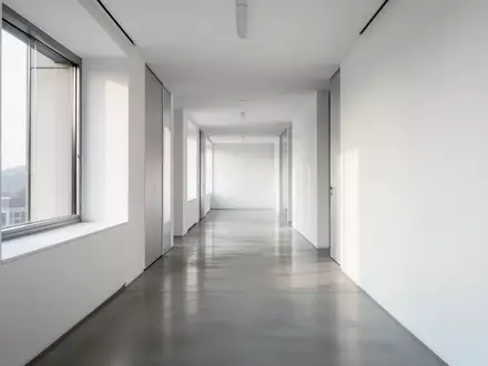 Ein leerer, modern gestalteter Büroflur mit klaren architektonischen Linien und hellem Tageslicht. - Foto: über boerse-global.de