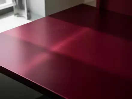 Eine Nahaufnahme einer gebürsteten, dunkelroten Aluminiumoberfläche in einem minimalistischen, industriellen Arbeitsumfeld. - Foto: über boerse-global.de