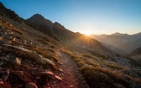 Ein sonnenbeschienener Bergpfad in einer alpinen Gebirgslandschaft bei Sonnenaufgang. - Foto: über boerse-global.de