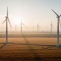 Großer Windpark in einer weiten Agrarlandschaft bei Sonnenaufgang mit mehreren Windkraftanlagen. - Foto: über boerse-global.de