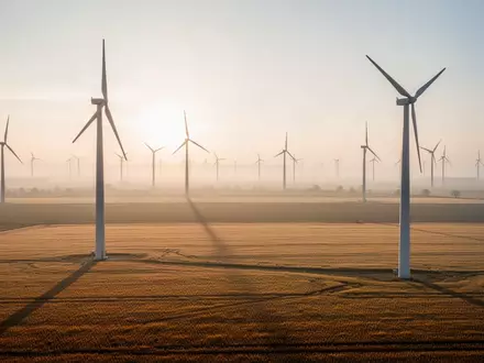 Großer Windpark in einer weiten Agrarlandschaft bei Sonnenaufgang mit mehreren Windkraftanlagen. - Foto: über boerse-global.de