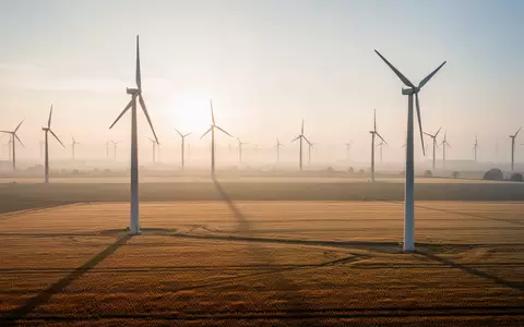 Großer Windpark in einer weiten Agrarlandschaft bei Sonnenaufgang mit mehreren Windkraftanlagen. - Foto: über boerse-global.de