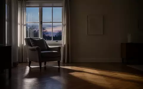 Ein ruhiges, spärlich beleuchtetes Wohnzimmer in der Abenddämmerung mit einem Sessel am Fenster. - Foto: über boerse-global.de