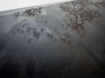 Nahaufnahme einer dunklen Metalloberfläche mit subtilen Abnutzungsspuren und ungleichmäßiger Textur bei diffusem Licht. - Foto: über boerse-global.de
