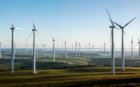 WeitlĂ€ufige Windkraftanlagen in einer grĂŒnen HĂŒgellandschaft bei klarem Tageslicht. - Foto: ĂŒber boerse-global.de