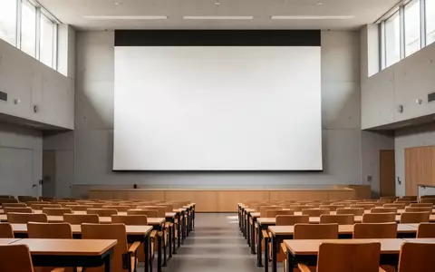 Ein leerer, modern gestalteter Hörsaal in einer Universität mit einer leeren Projektionsfläche und natürlichem Lichteinfall. - Foto: über boerse-global.de