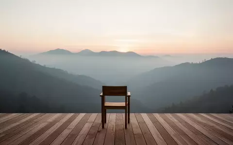 Eine minimalistische Holzterrasse mit Blick auf ein nebliges Gebirge bei Sonnenaufgang, die Stille und Erholung vermittelt. - Foto: über boerse-global.de