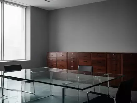 Ein minimalistisches, leeres Büro mit einem gläsernen Besprechungstisch und hölzernen Aktenschränken im Hintergrund. - Foto: über boerse-global.de