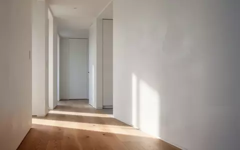 Ein minimalistischer, moderner Wohnungsflur mit klaren weißen Wänden und natürlichem Licht, das sanfte Schatten auf einen Eichenholzboden wirft. - Foto: über boerse-global.de