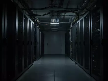 Dunkler, minimalistischer Serverraum mit metallischen Strukturen und Schatten in einer ruhigen, menschenleeren Umgebung. - Foto: über boerse-global.de