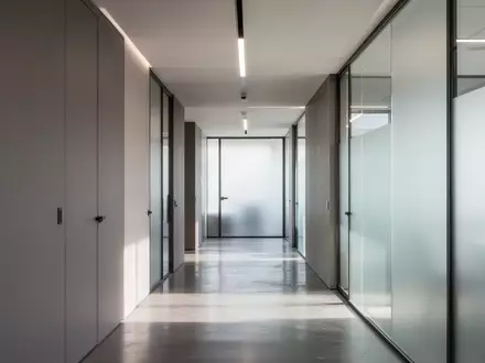 Ein minimalistischer, moderner Büroflur mit klaren Linien und indirektem Tageslicht, der eine professionelle und sichere Umgebung symbolisiert. - Foto: über boerse-global.de