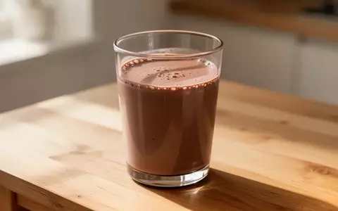 Ein Glas Schokoladenmilch auf einer schlichten Holzoberfläche in hellem, natürlichem Tageslicht. - Foto: über boerse-global.de