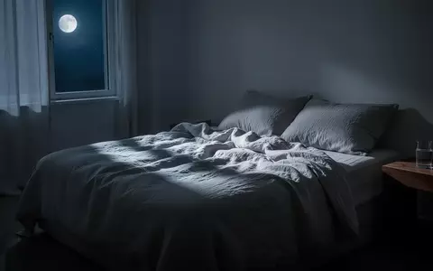 Ein minimalistisch eingerichtetes Schlafzimmer bei Nacht mit sanftem Mondlicht, das durch ein Fenster fällt. - Foto: über boerse-global.de