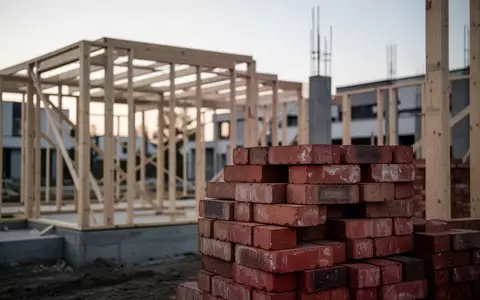 Eine Baustelle mit Ziegelsteinen und einem Holzrahmen bei Dämmerung als Symbol für Immobilienkäufe. - Foto: über boerse-global.de