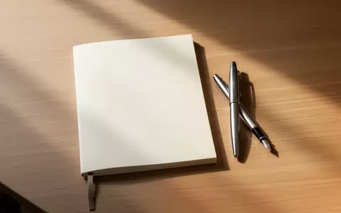 Ein leeres Notizbuch und ein Füllfederhalter liegen ordentlich auf einem hölzernen Schreibtisch in sanftem Morgenlicht. - Foto: über boerse-global.de