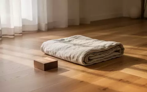 Eine minimalistische, lichtdurchflutete Räumlichkeit mit einer ordentlich gefalteten Decke und einem Holzblock auf einem Holzboden. - Foto: über boerse-global.de