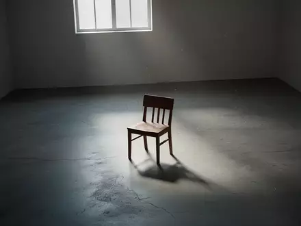 Ein einsamer Holzstuhl in einem leeren, minimalistisch beleuchteten Raum, der eine Atmosphäre von Introspektion und Rückzug vermittelt. - Foto: über boerse-global.de
