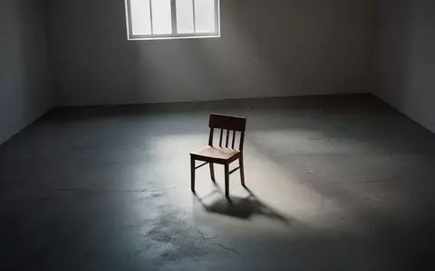 Ein einsamer Holzstuhl in einem leeren, minimalistisch beleuchteten Raum, der eine Atmosphäre von Introspektion und Rückzug vermittelt. - Foto: über boerse-global.de