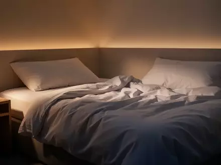 Ein minimalistisches, in warmes Licht getauchtes Schlafzimmer am Abend mit einem ungemachten Bett. - Foto: über boerse-global.de