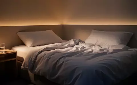 Ein minimalistisches, in warmes Licht getauchtes Schlafzimmer am Abend mit einem ungemachten Bett. - Foto: über boerse-global.de