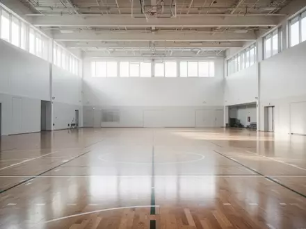 Leere, helle Sporthalle mit Parkettboden und hohen Fenstern als Symbol für kommunale Bewegungsangebote im Winter. - Foto: über boerse-global.de