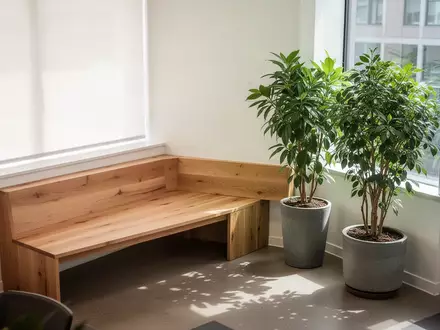 Ein heller, minimalistischer Pausenraum mit einer Holzbank und einer großen Pflanze, der eine ruhige Arbeitsumgebung symbolisiert. - Foto: über boerse-global.de