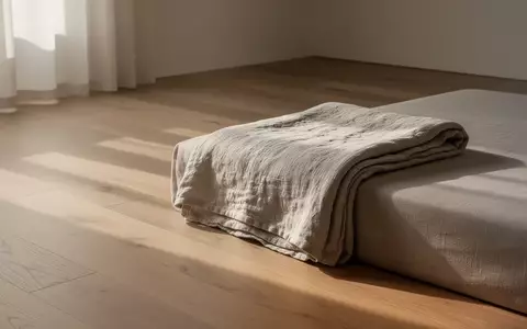 Ein minimalistisch eingerichteter, ruhiger Raum mit einer gefalteten Decke in sanftem Tageslicht. - Foto: ĂŒber boerse-global.de