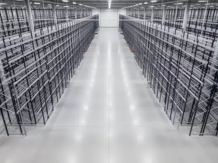 Weite, leere Lagerhalle mit hohen Regalsystemen und poliertem Industrieboden in einer automatisierten Logistikanlage. - Foto: über boerse-global.de