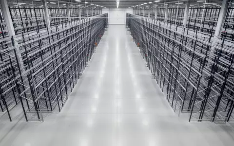 Weite, leere Lagerhalle mit hohen Regalsystemen und poliertem Industrieboden in einer automatisierten Logistikanlage. - Foto: über boerse-global.de