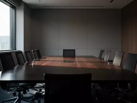 Ein leerer, modern gestalteter Konferenzraum mit einem dunklen Holztisch und ergonomischen Stühlen in gedämpftem Licht. - Foto: über boerse-global.de