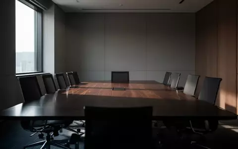 Ein leerer, modern gestalteter Konferenzraum mit einem dunklen Holztisch und ergonomischen Stühlen in gedämpftem Licht. - Foto: über boerse-global.de