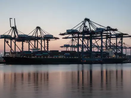 Ein moderner Industriehafen mit Containerkränen bei Dämmerung als Symbol für den deutschen Außenhandel. - Foto: über boerse-global.de